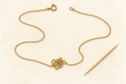 Illustration of an unclasped necklace resting flat with slack around a tangle and a wooden toothpick beside it.