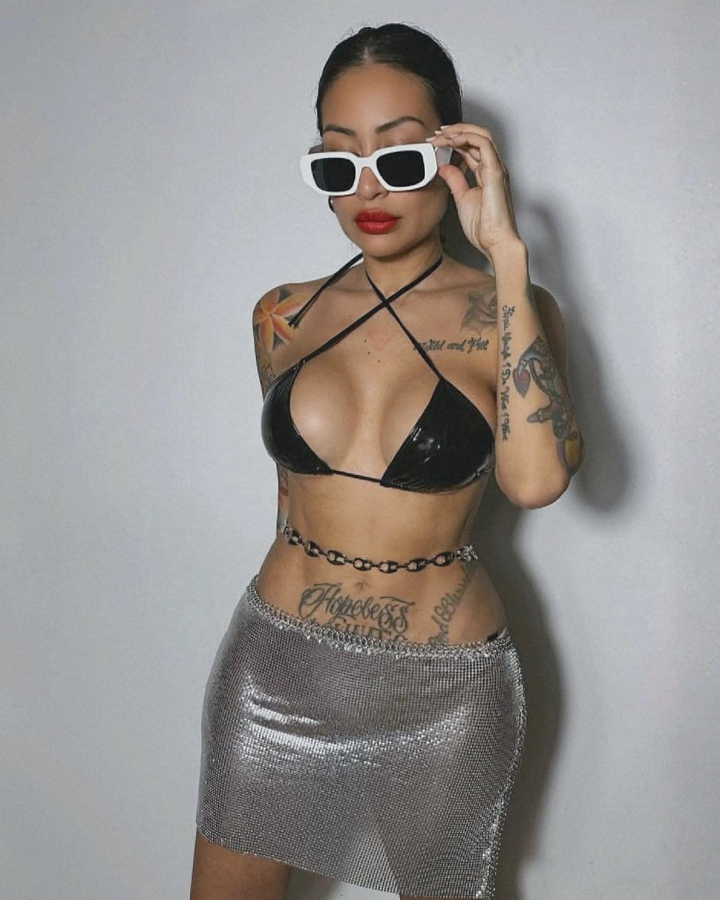Woman wearing a black bikini top and silver skirt with sunglasses on a plain background
